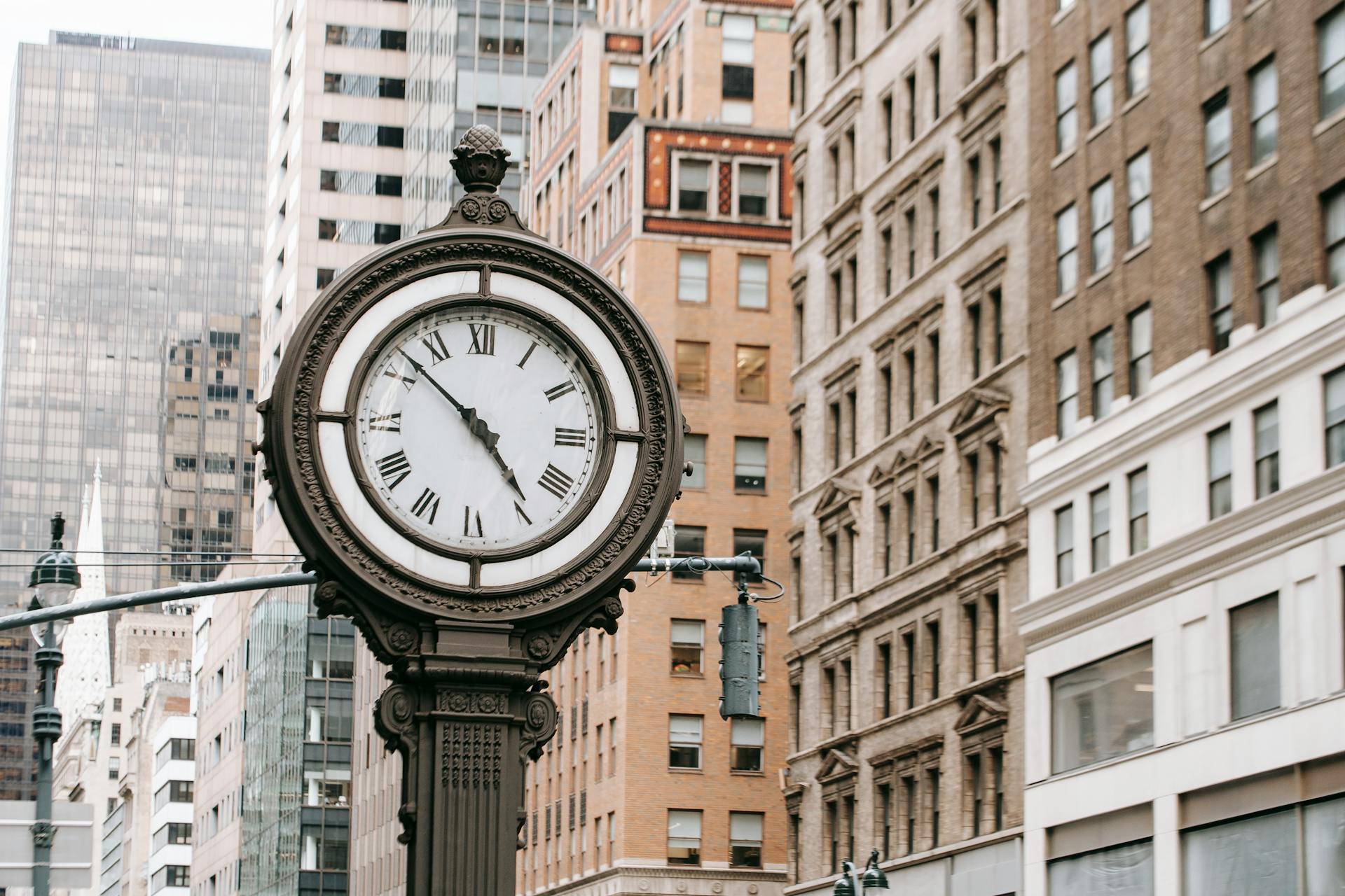 Vintage street clock on pillar located near residential buildings and skyscrapers in downtown of New York city in financial district