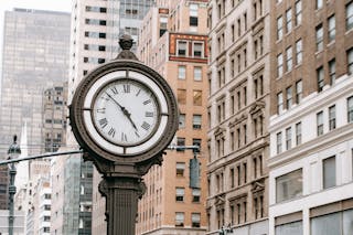 Vintage street clock on pillar located near residential buildings and skyscrapers in downtown of New York city in financial district