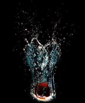 A red apple creating a splash in water against a black background, showcasing dynamic motion.