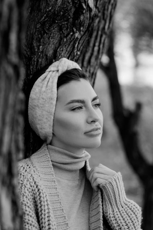 Free Grayscale Photo of Woman in Knit Sweater and Headband Leaning on Tree Stock Photo