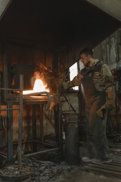 Free A blacksmith in a workshop carefully handling molten metal near a glowing forge. Stock Photo
