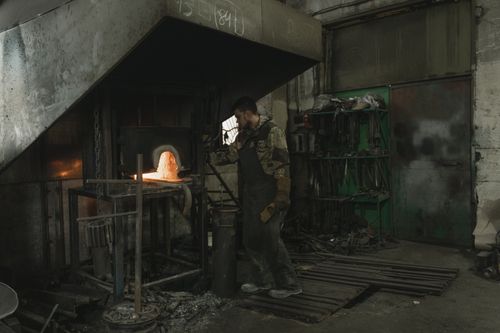 Free Blacksmith working at a glowing forge, shaping heated metal in an industrial setting. Stock Photo