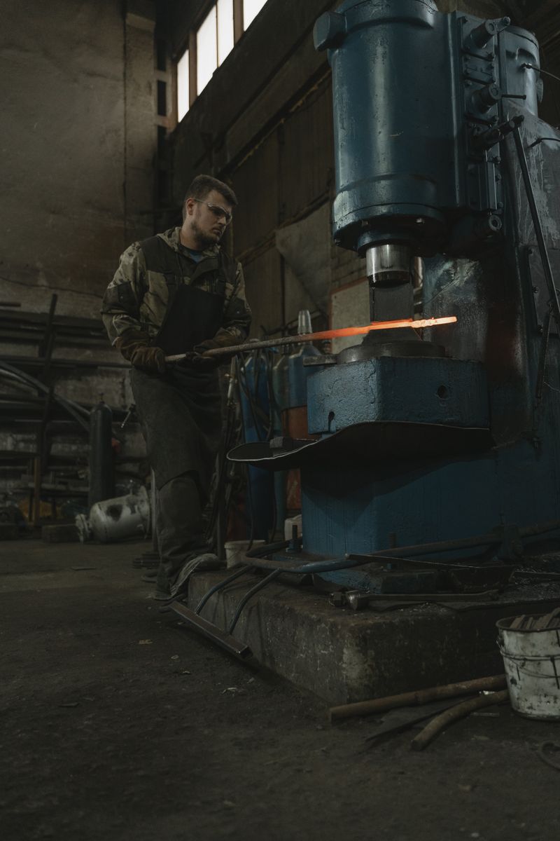 Metalsmith working steel with hydraulic press indoors for industrial metalwork