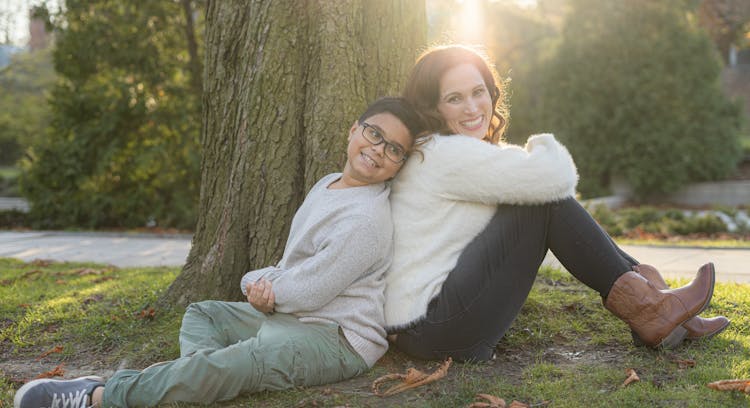 Portrait Of Happy Mother And Son Sitting Under Tree