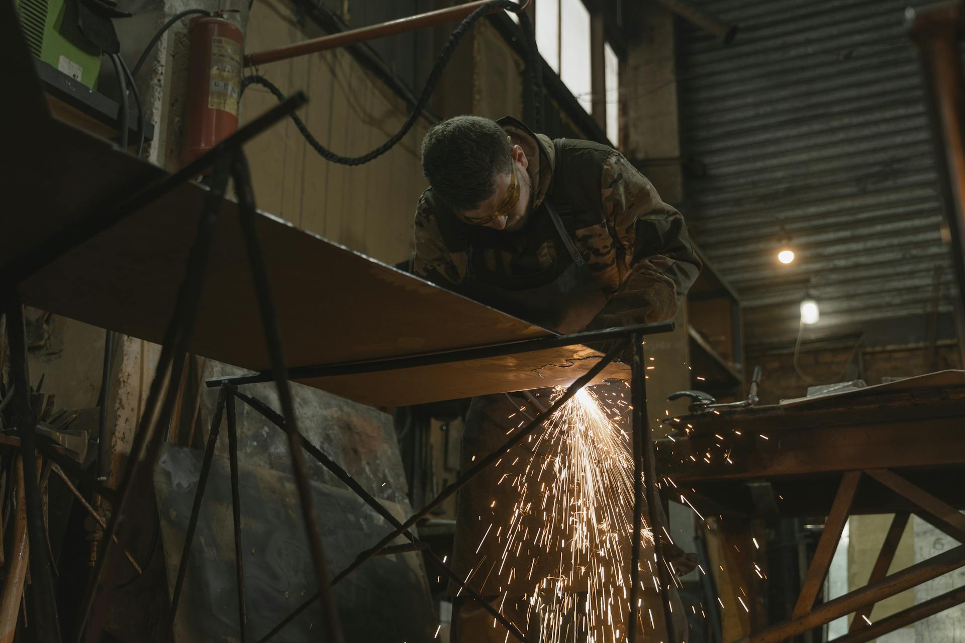 A worker focused on welding metal inside an industrial setting with sparks flying.