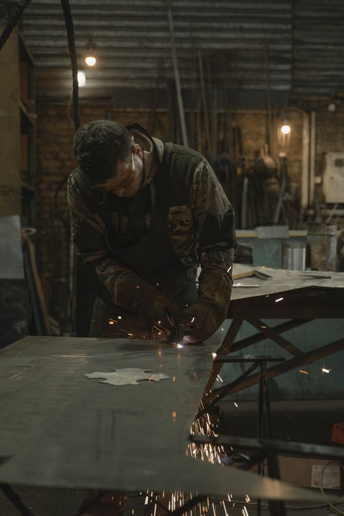 Free A welder sparks metal in a busy industrial workshop setting. Stock Photo