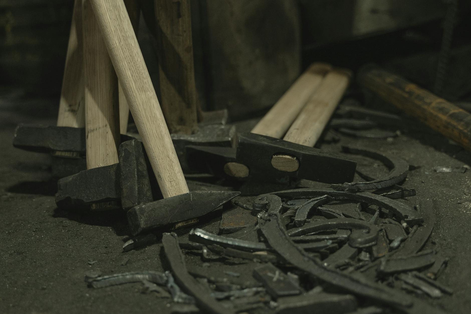 Close-up of hammers with wooden handles and metal scrap in a workshop setting.
