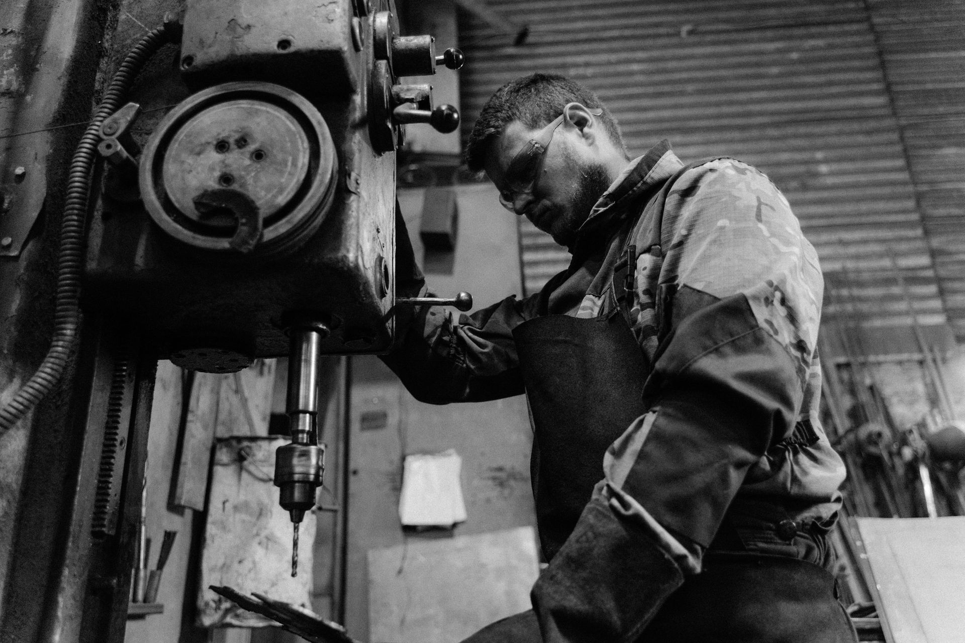 Black and white photo of a worker focused on operating a drill press, emphasizing craftsmanship.
