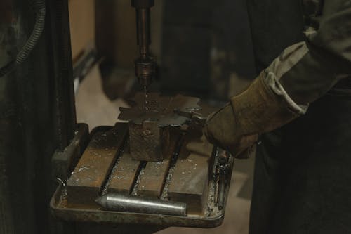 Person in Brown Safety Gloves Holding Metal on a Drilling Machine