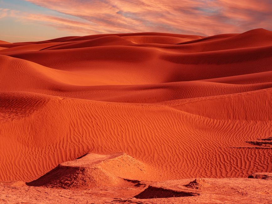 Explore vibrant red sand dunes with dramatic skies, creating a stunning natural desert landscape.