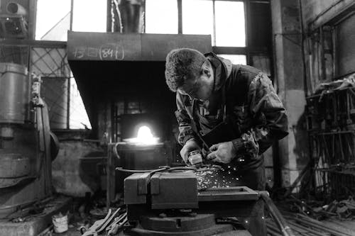 Grayscale Photo of a Man Doing a Metalwork