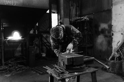 Grayscale Photo of a Man Doing a Metalwork