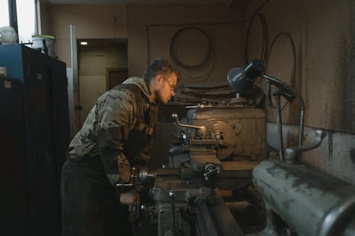 Man in Green and Brown Camouflage Jacket Using Black and Silver Power Tool