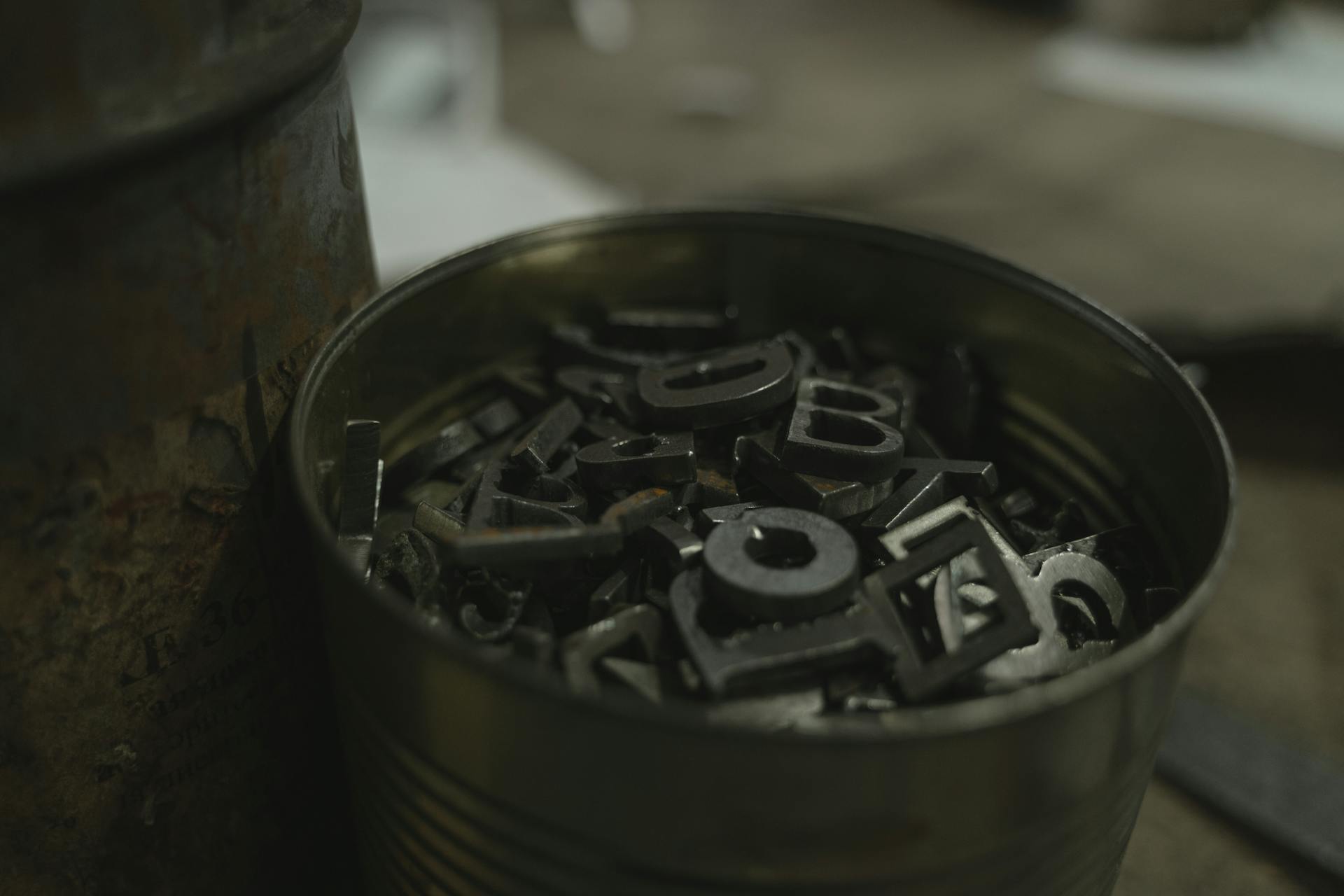 A bucket of metal letter stamps in an indoor industrial environment.