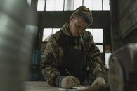 Man in Brown and Black Camouflage Jacket Writing on White Paper