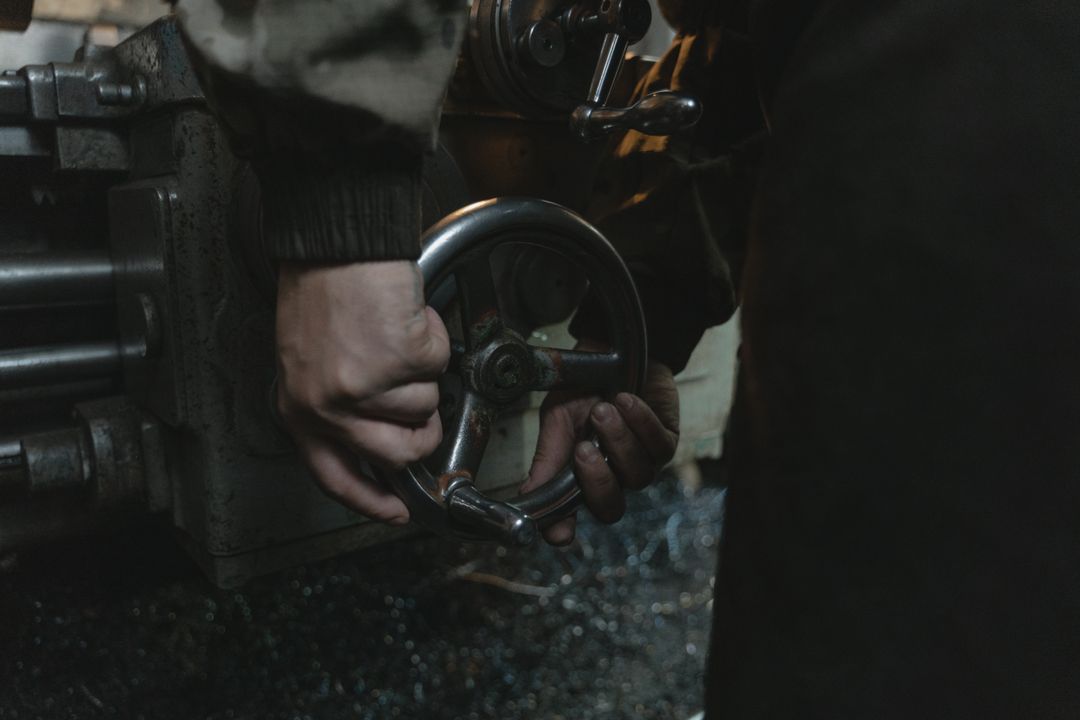 Close-up of a man's hands gripping a metal handwheel in a dim workshop