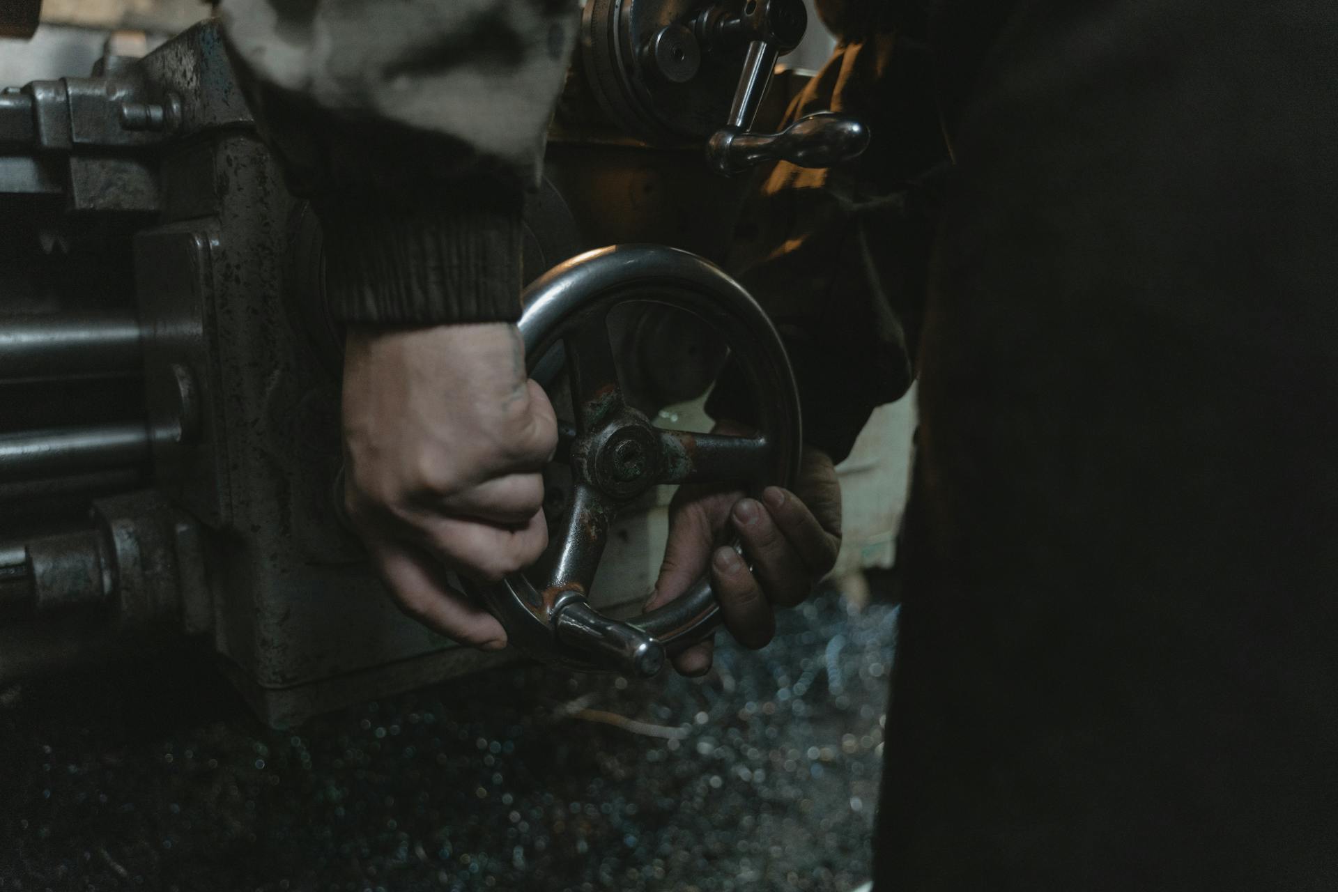 Close-up of hands operating a lathe machine in a workshop, showcasing precision metalwork.
