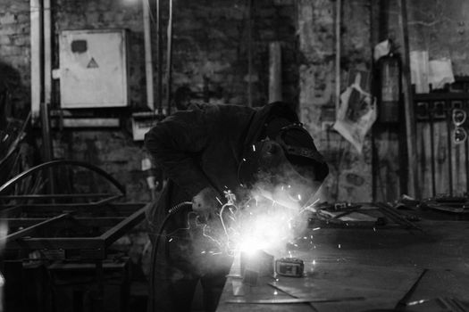 A monochrome image of a welder performing metalwork with sparks flying in an industrial workshop.