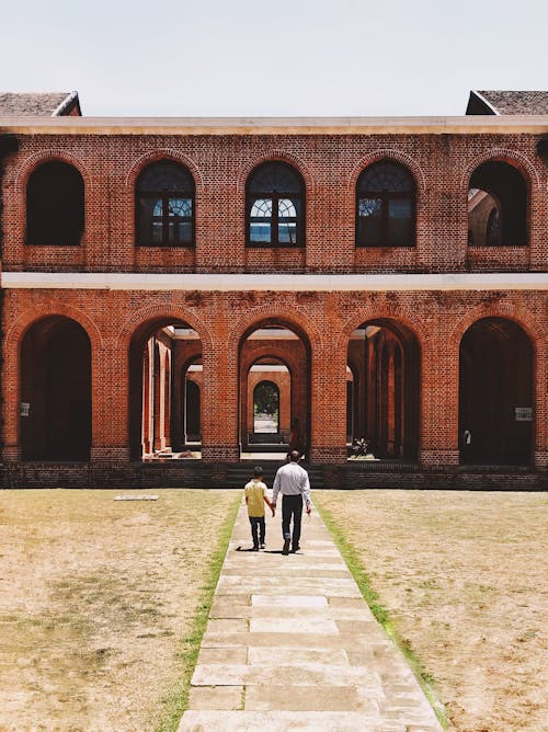 Father and Son Holding Hands and Walking Towards a Red Brick Building 