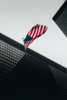 Low angle shot of American flag waving amidst modern skyscraper architecture.
