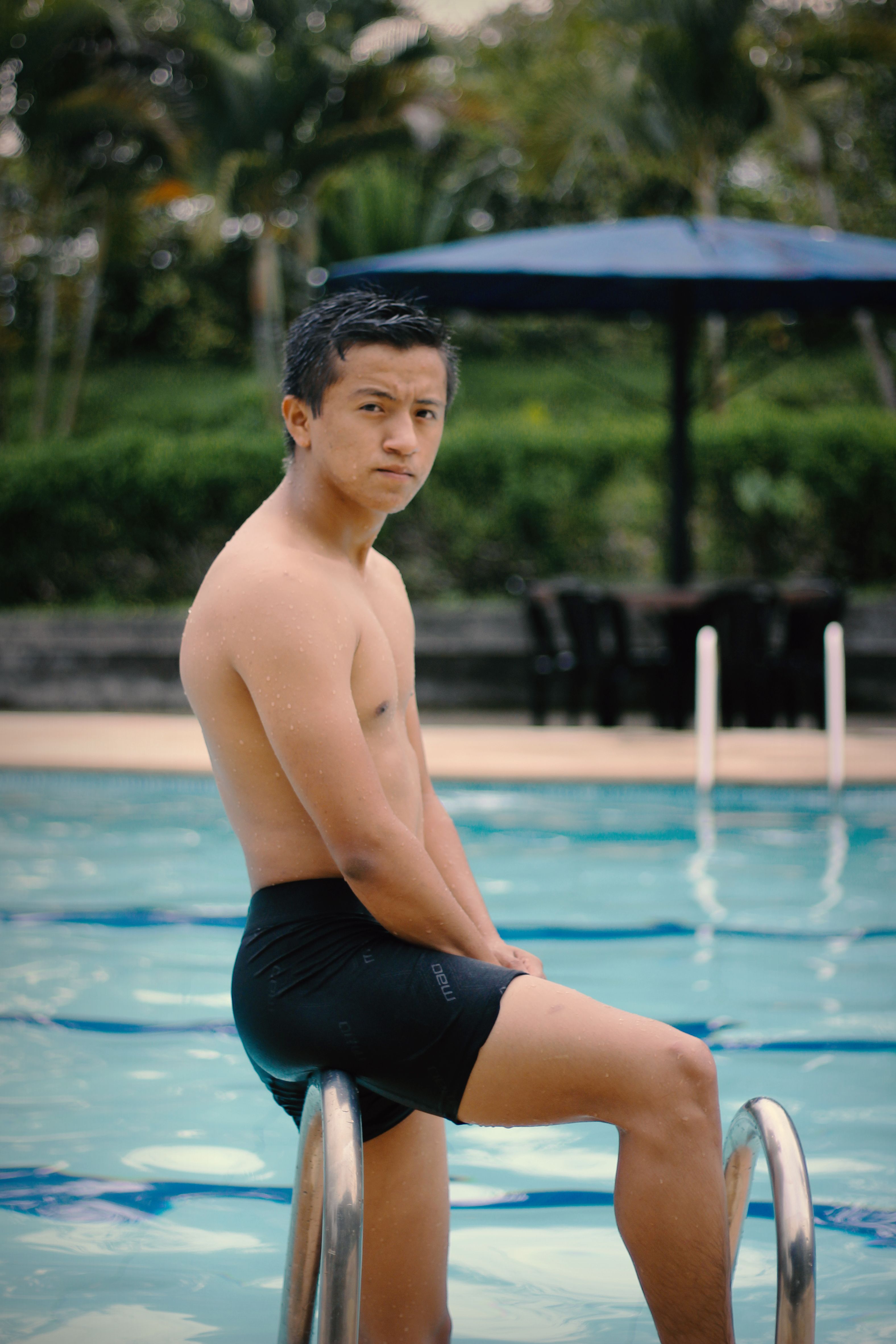 A shirtless young man poses by the pool, showcasing confidence and leisure.