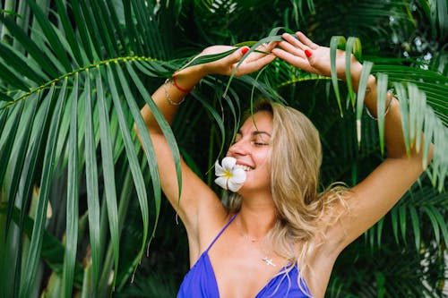 Free Woman Biting a Flower Standing Under Palm Leaves Stock Photo