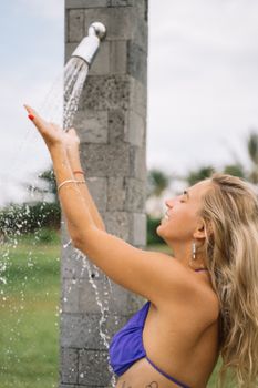 Woman with blond hair enjoying a refreshing outdoor shower under a clear blue sky.