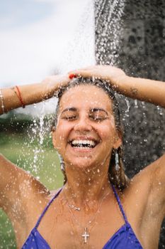 Happy woman enjoying an outdoor shower on a warm day with a bright smile.