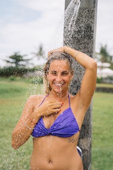 阳光明媚的日子里，一位穿着比基尼的微笑女子正享受着清爽的户外淋浴