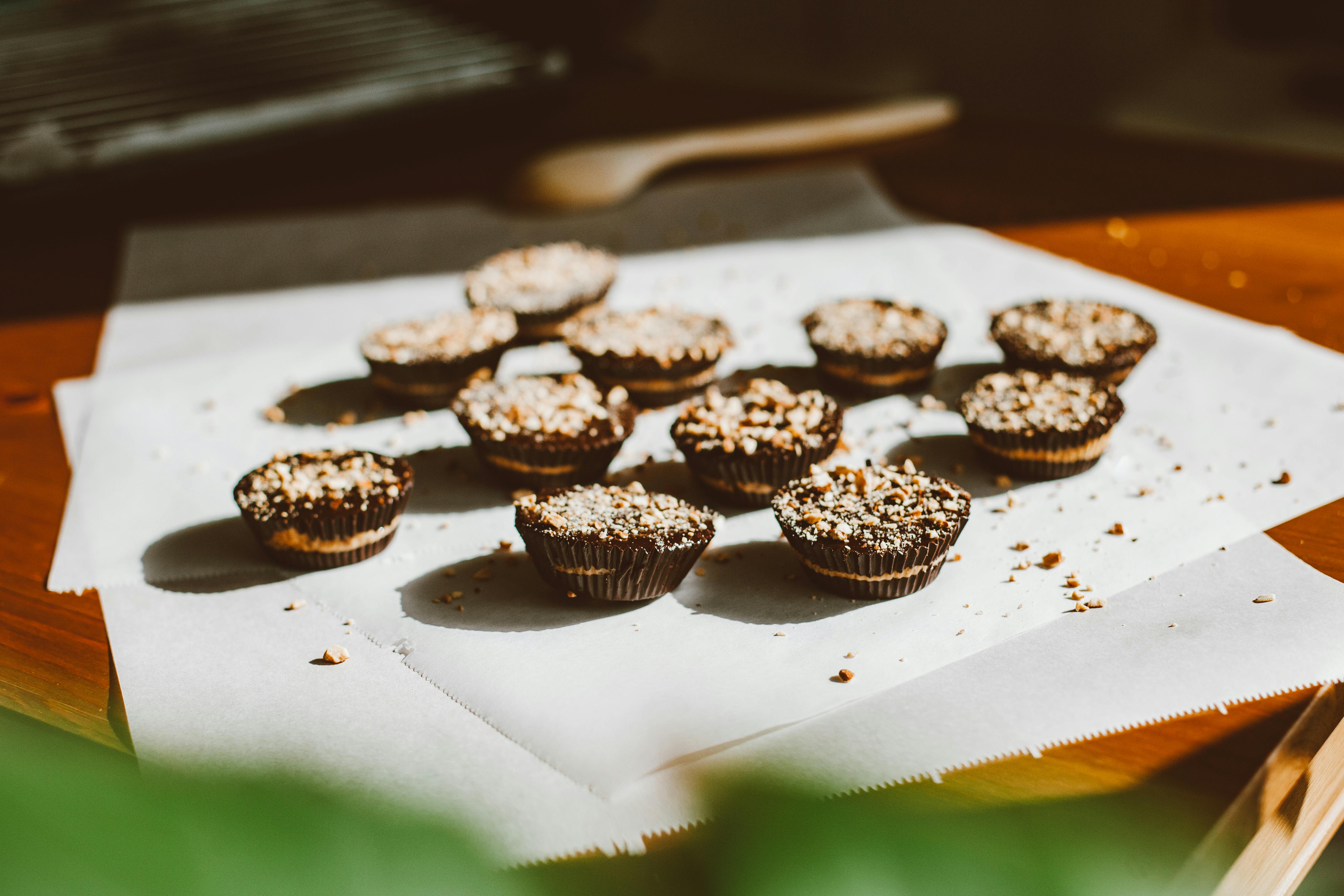 Close-up of chocolate cupcakes topped with chopped nuts on parchment paper in warm natural light
