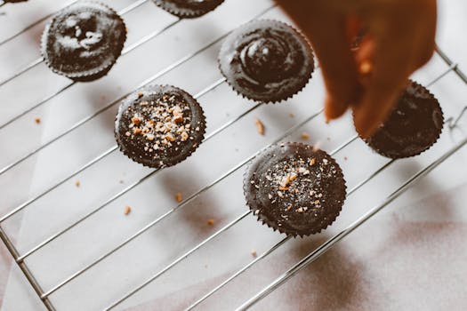 Freshly baked chocolate muffins sprinkled with nuts on a cooling rack, a hand arranging them.