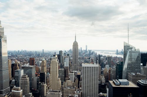 Free Drone view of empire state building located amidst high rise buildings on Manhattan in New York city against cloudy sky Stock Photo