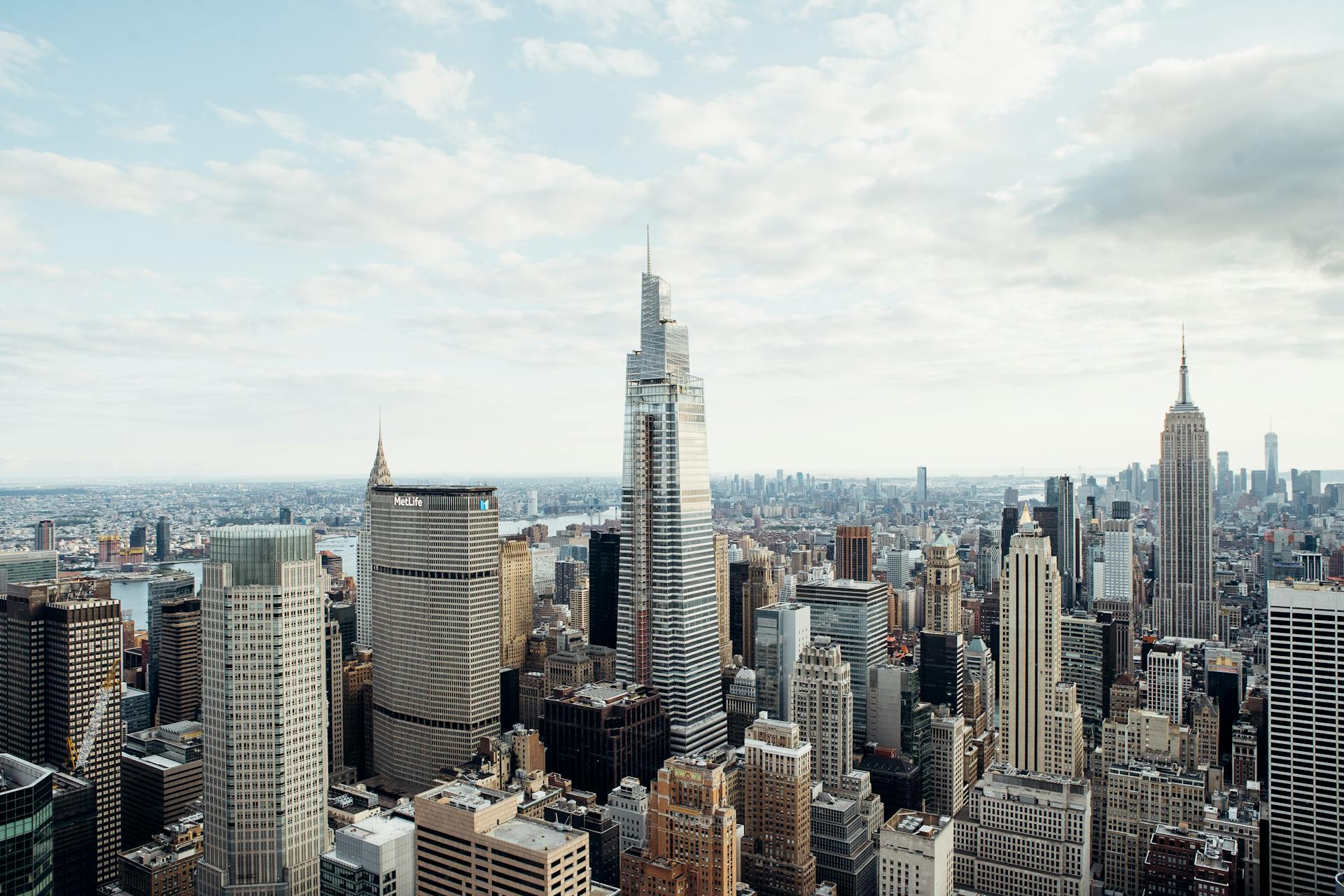 Drone view of modern high rise houses and empire state building located against cloudy sky in downtown of New York city