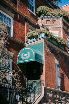 Low angle of door with awning of aged brick building with stairs located in residential district against blue sky in sunlight