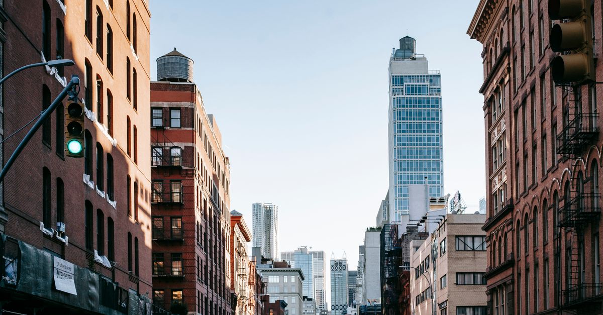 District of New York with aged residential buildings and modern commercial skyscrapers against cloudless blue sky