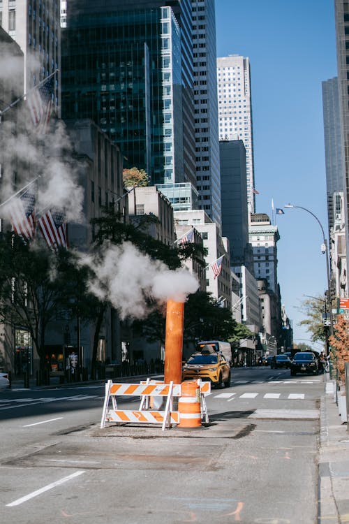 Orange stream pipe located on asphalt road between modern skyscrapers against cloudless blue sky in New York