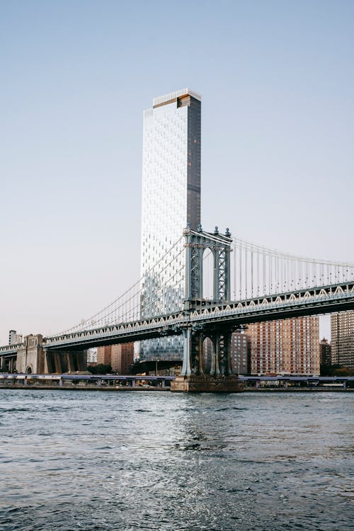 Glass skyscraper behind suspension bridge and river