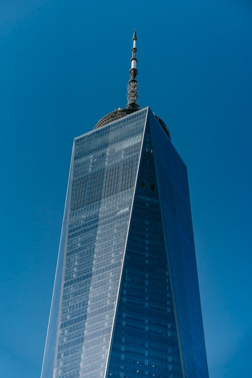 From below of glass facade of high rise building with tower on roof against clear blue sky