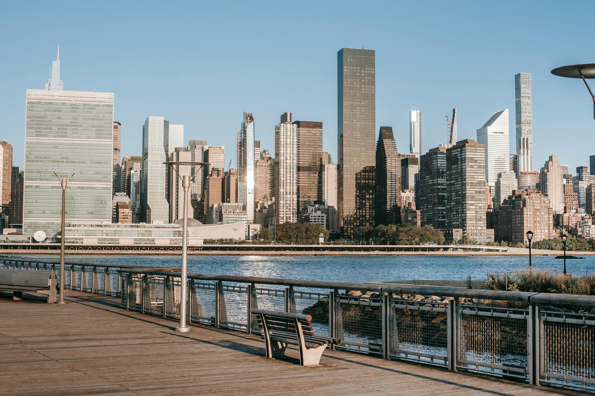 Sunny view of New York City skyline and waterfront promenade, capturing the modern cityscape.