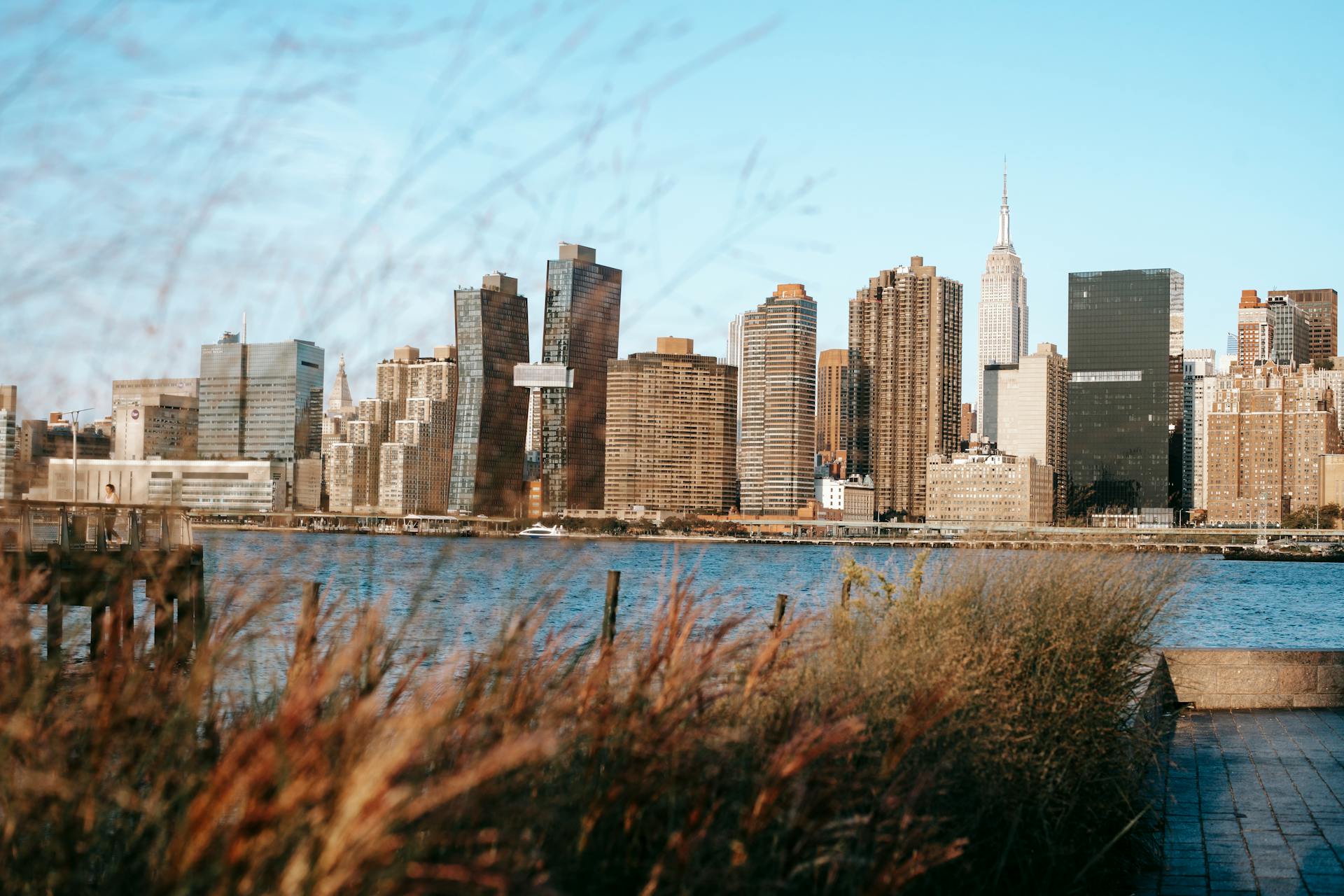 Calm Hudson River flowing near modern district with high rise buildings placed in New York under cloudless blue sky in daytime