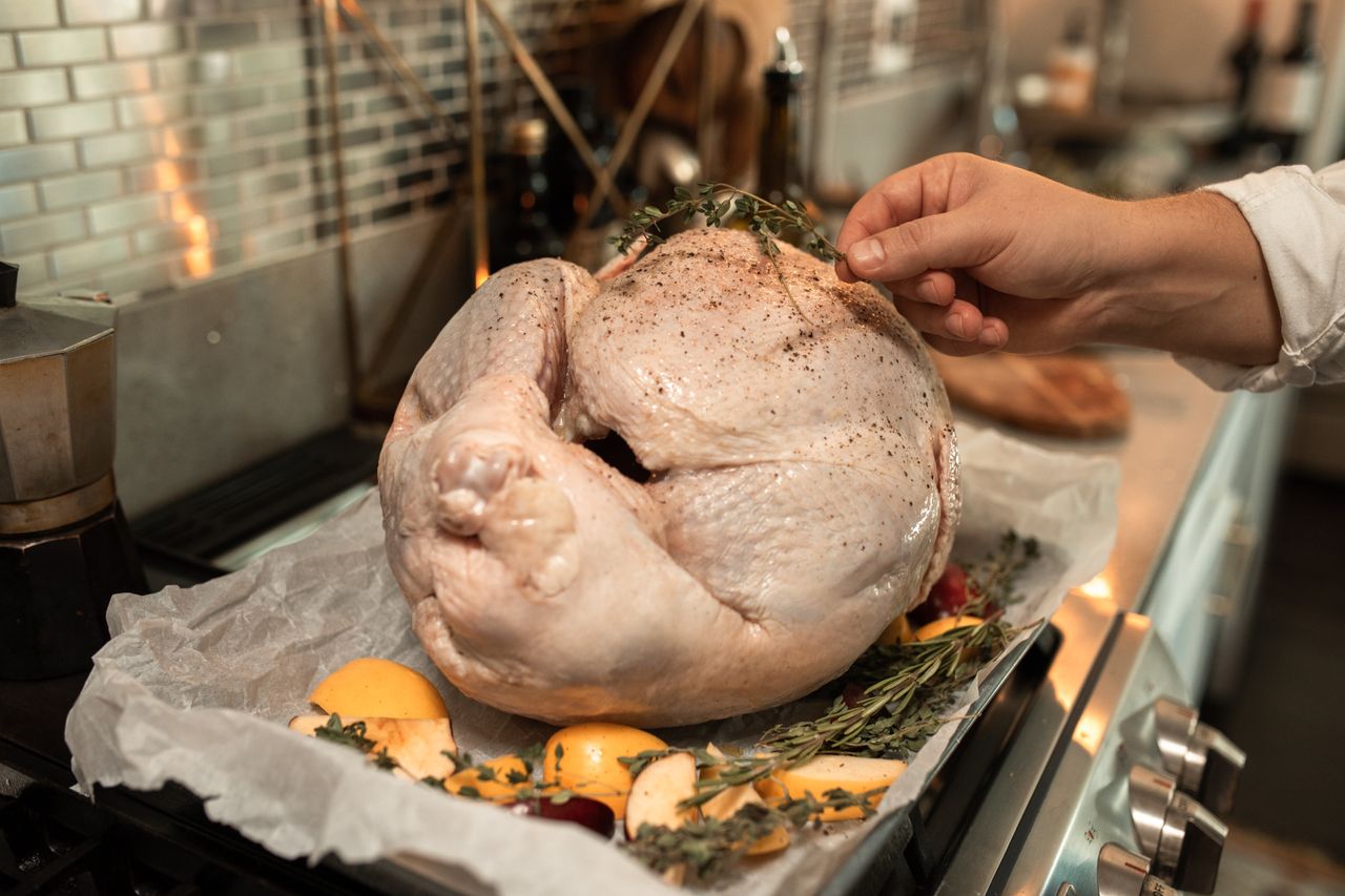 Hand placing fresh herbs on a raw seasoned Thanksgiving turkey in a kitchen