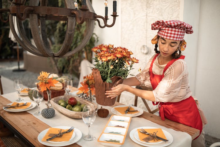 A Woman Placing Potted Flowers On A Dining Table