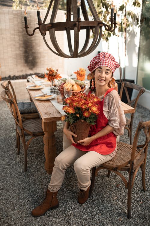 Free Smiling woman in fall attire holding chrysanthemums at an outdoor family gathering table. Stock Photo