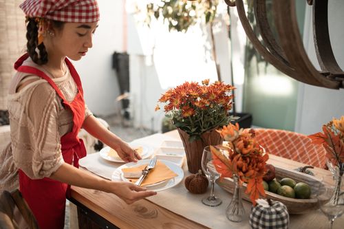 Free Woman setting a table with autumn decorations and flowers indoors. Stock Photo