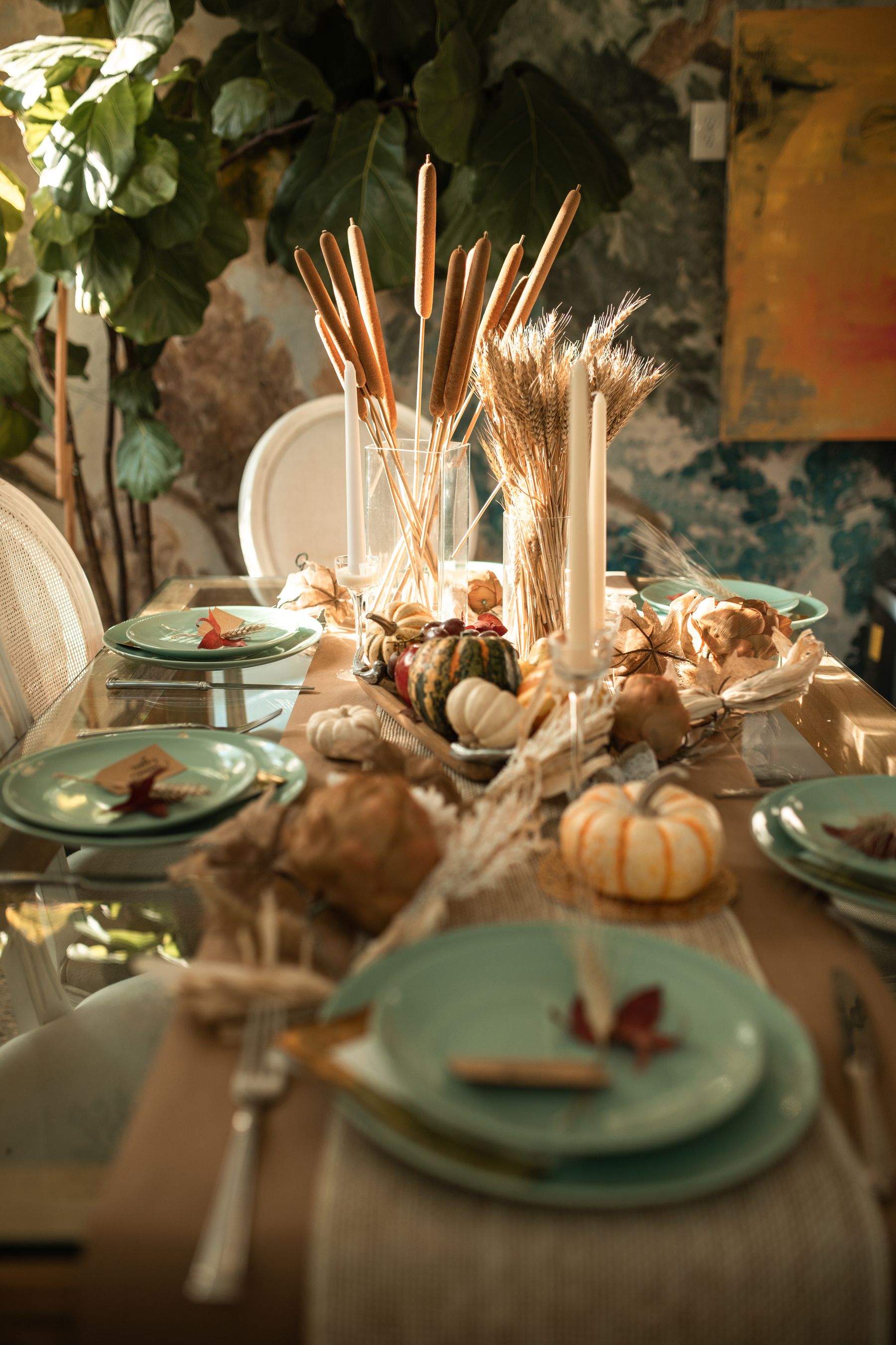 Thanksgiving table arranged with green plates, gourds and tall dried stems