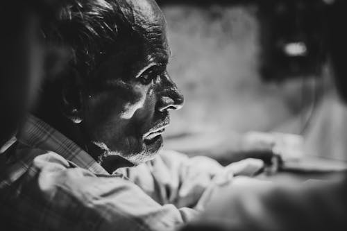 Side view of crop black and white thoughtful middle aged ethnic male in casual clothes sitting on street and looking away pensively