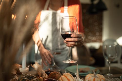 Free Cozy indoor autumn dinner setting with a person holding a glass of red wine, surrounded by festive decor. Stock Photo