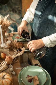 A person pours red wine into a decanter on an autumn-themed dinner table, creating a cozy atmosphere.
