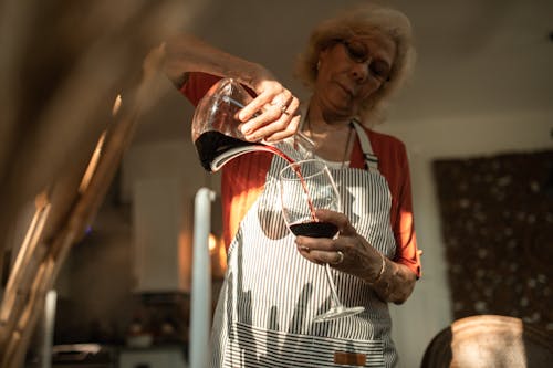 An Elderly Woman Pouring Wine into a Glass