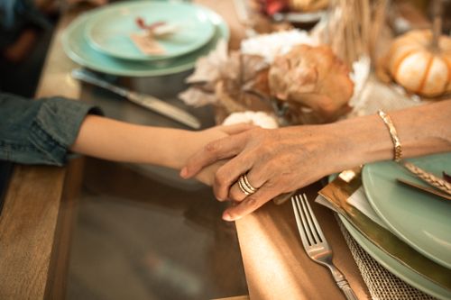 Free Close-up of an intergenerational handhold at a cozy Thanksgiving dinner table. Stock Photo